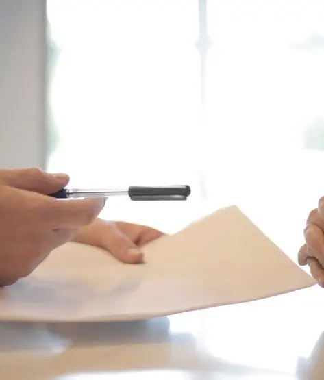 Une main tenant un stylo au-dessus d'une feuille de papier tendue à une autre personne